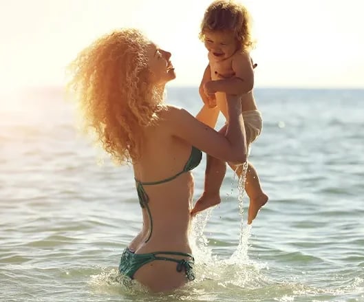 Mother lifting her young child at the beach, the family stage mommy makeover timing depends on